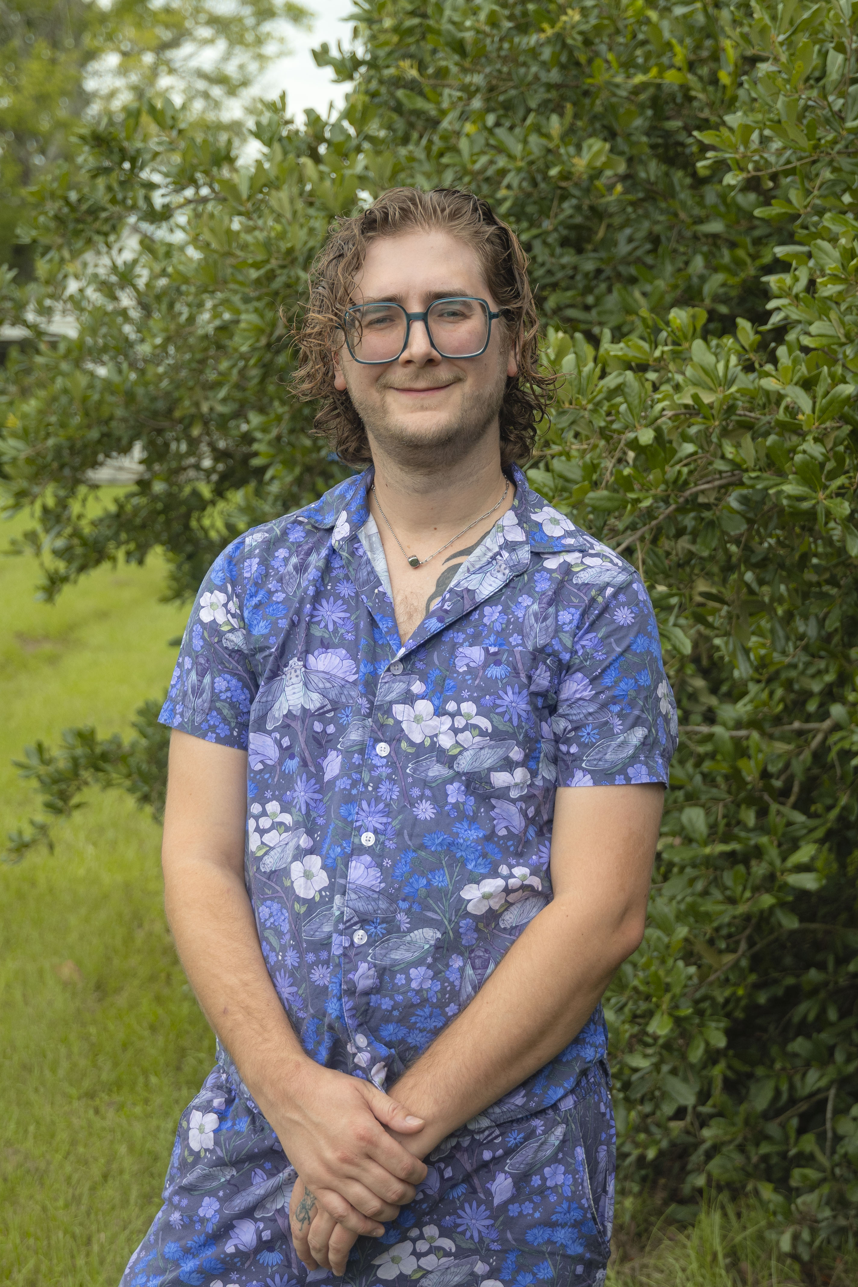 Image of Male, Damian Tweedy, Fluker's Larva Production Scientist, in blue outfit in front of trees