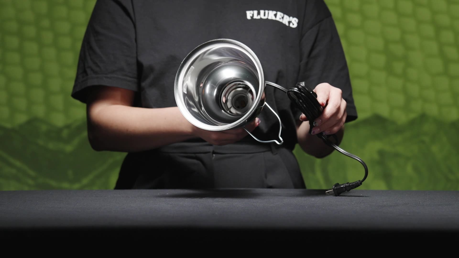 Person in black Fluker's t-shirt holding fluker's Deep Dome Lamp showing the inside of the aluminum reflector without bulb inserted