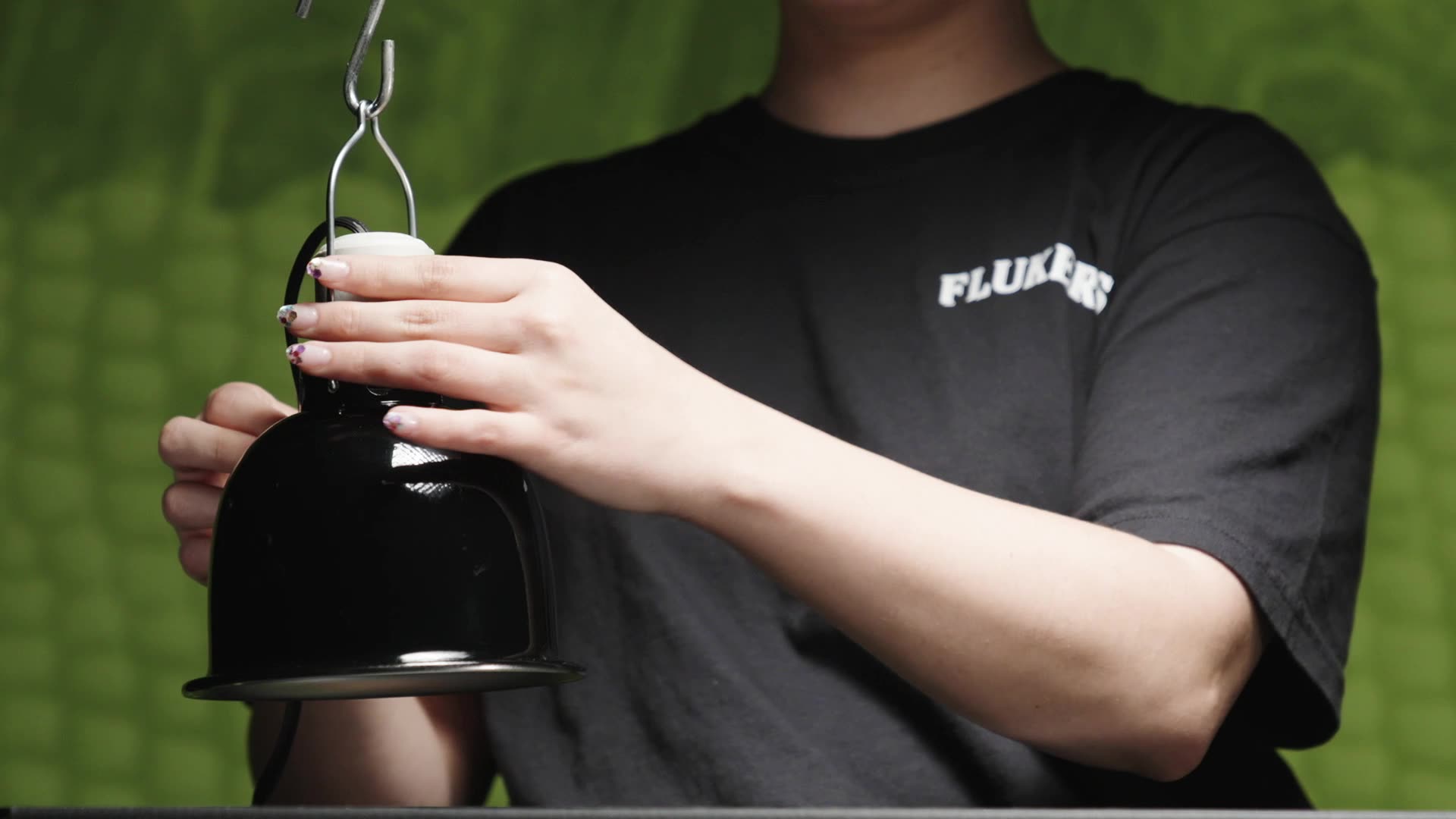 Image of person holding Fluker's Deep Dome Lamp in hands, attaching it to a lamp stand on green background